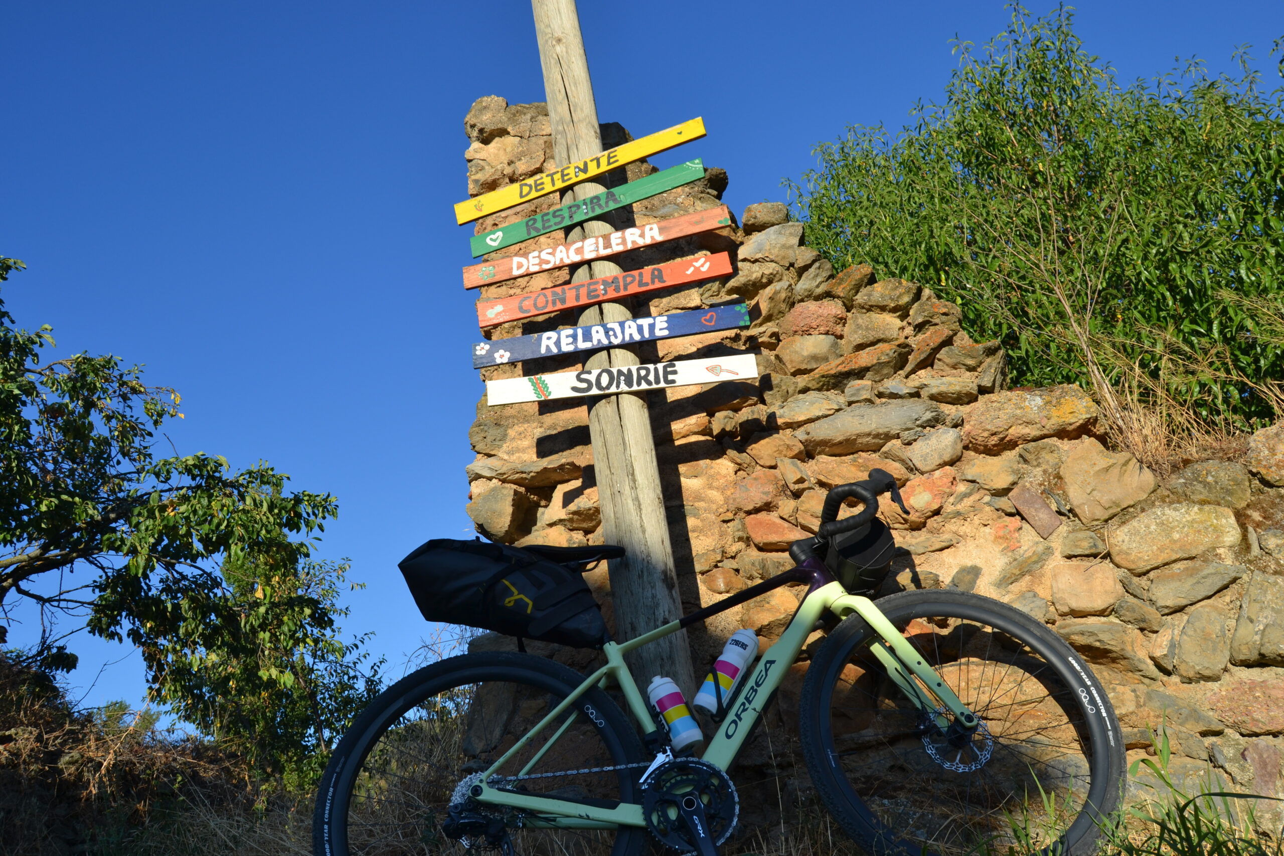 Bicicleta de bikepacking apoyada en un poste indicador de caminos junto a un muro de piedra